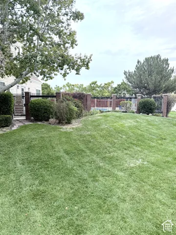 Expansive grassy area featuring mature landscaping and a black wrought iron fence with brick pillars