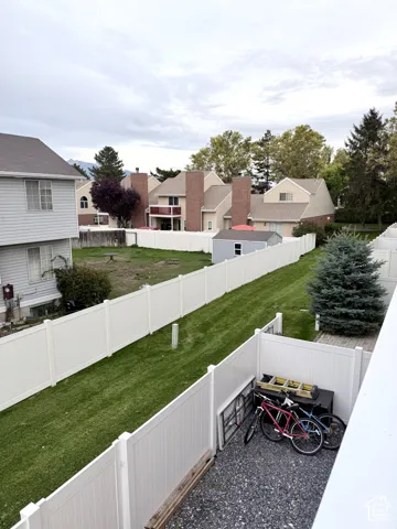 Expansive fenced yard featuring a manicured lawn, gravel patio, and mature evergreen tree