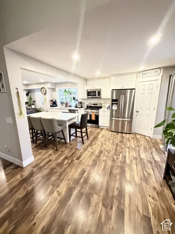 Open-concept kitchen featuring wood-finish flooring, white cabinetry, stainless steel appliances, a center island with seating, and recessed lighting