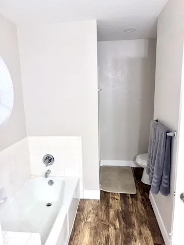 White tiled tub with chrome fixtures, wood-finish flooring, and recessed lighting