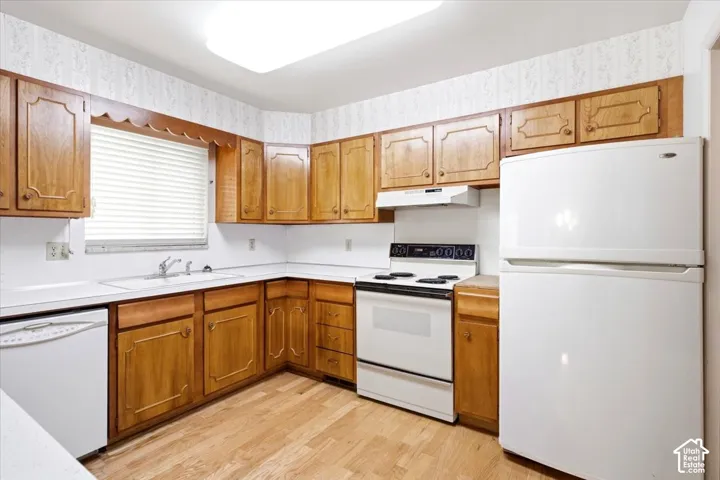 Kitchen featuring wood-finish cabinetry, white countertops, built-in sink, and white appliances including a refrigerator, range, and dishwasher