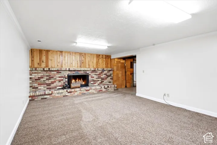 Carpeted room featuring a brick-surround fireplace with a wood panel accent wall and overhead lighting