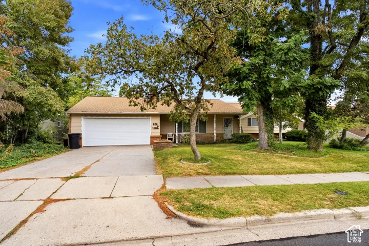 Ranch-style residence featuring a single-car garage, concrete driveway, and a front lawn with mature trees