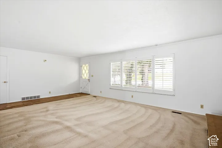 Spacious room featuring white walls, crown molding, and multiple windows with plantation shutters