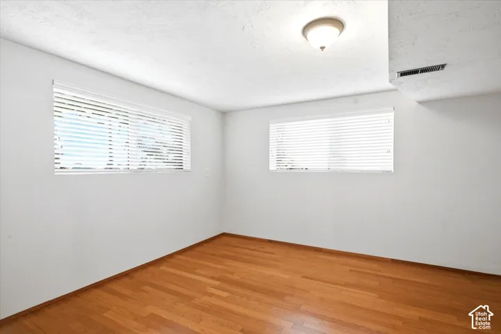 Wood-finish flooring with white walls, two windows featuring horizontal blinds, and a ceiling-mounted light fixture