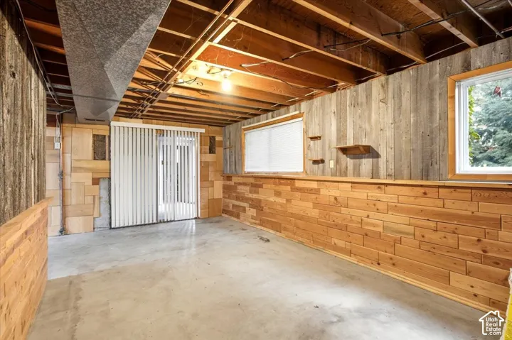 Spacious basement featuring wood-finish wall paneling, exposed beam ceiling with recessed lighting, concrete flooring, and natural light from multiple windows