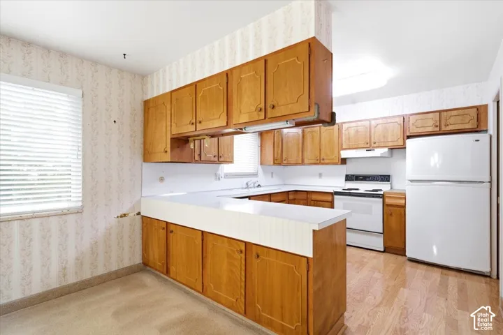 Wood-finish flooring, wood cabinetry, white countertops, built-in white appliances, and a window with blinds