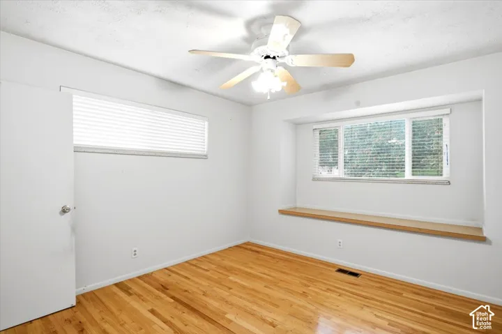 Hardwood flooring, ceiling fan with integrated lighting, large window with built-in wooden ledge, secondary horizontal window, white interior walls