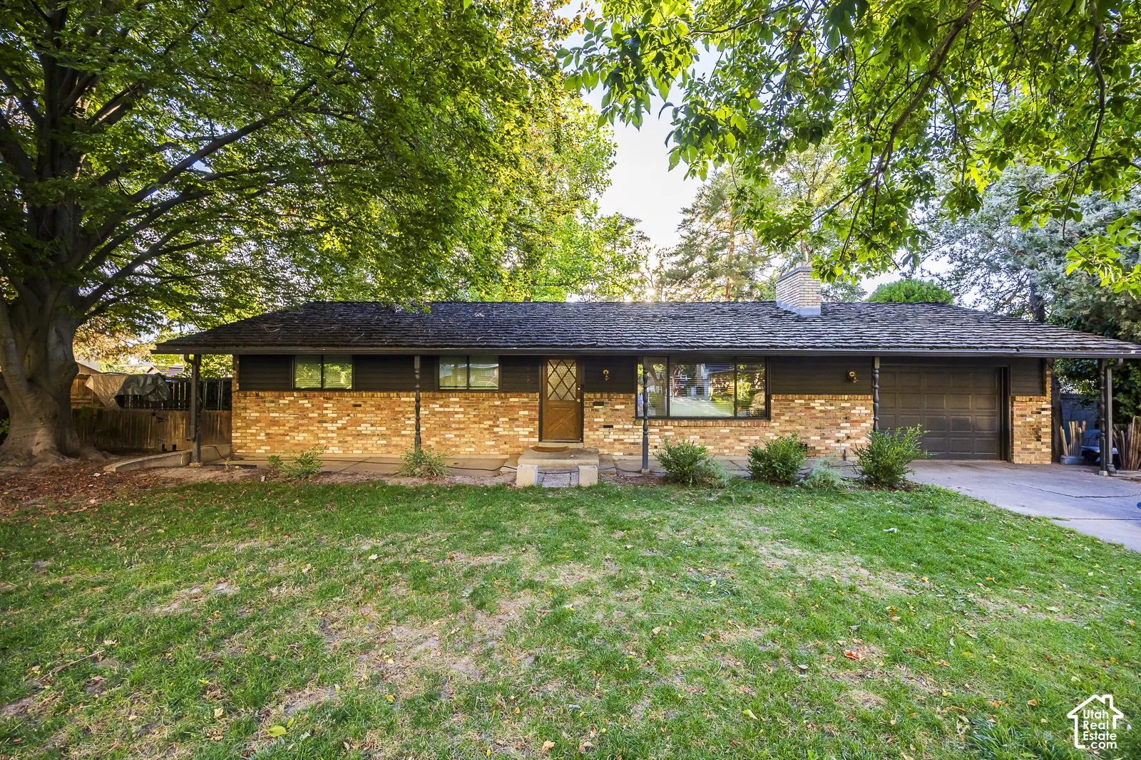 Brick facade with dark siding, single-car garage, front entry with storm door, and mature shade trees