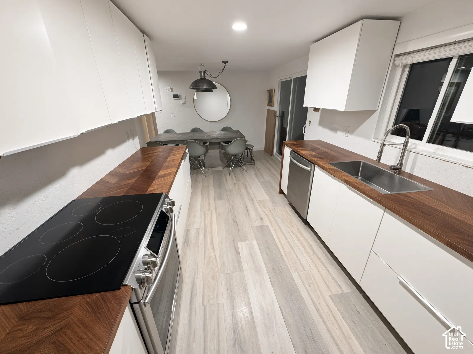 Kitchen featuring wood-finish countertops, stainless steel appliances, white flat-panel cabinetry, and light wood-finish flooring