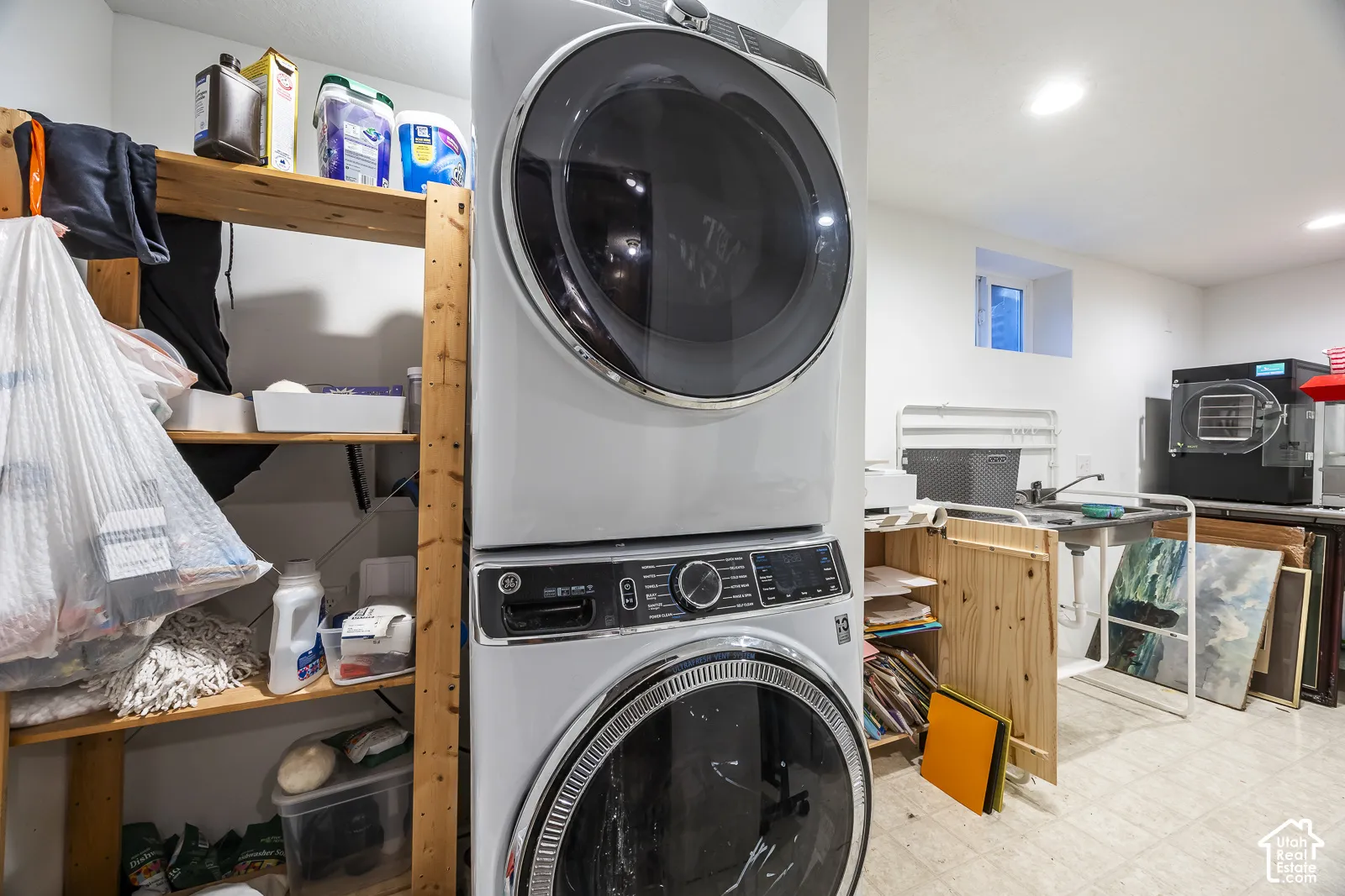 Laundry area featuring a stacked washer and dryer, wood shelving, and a utility sink