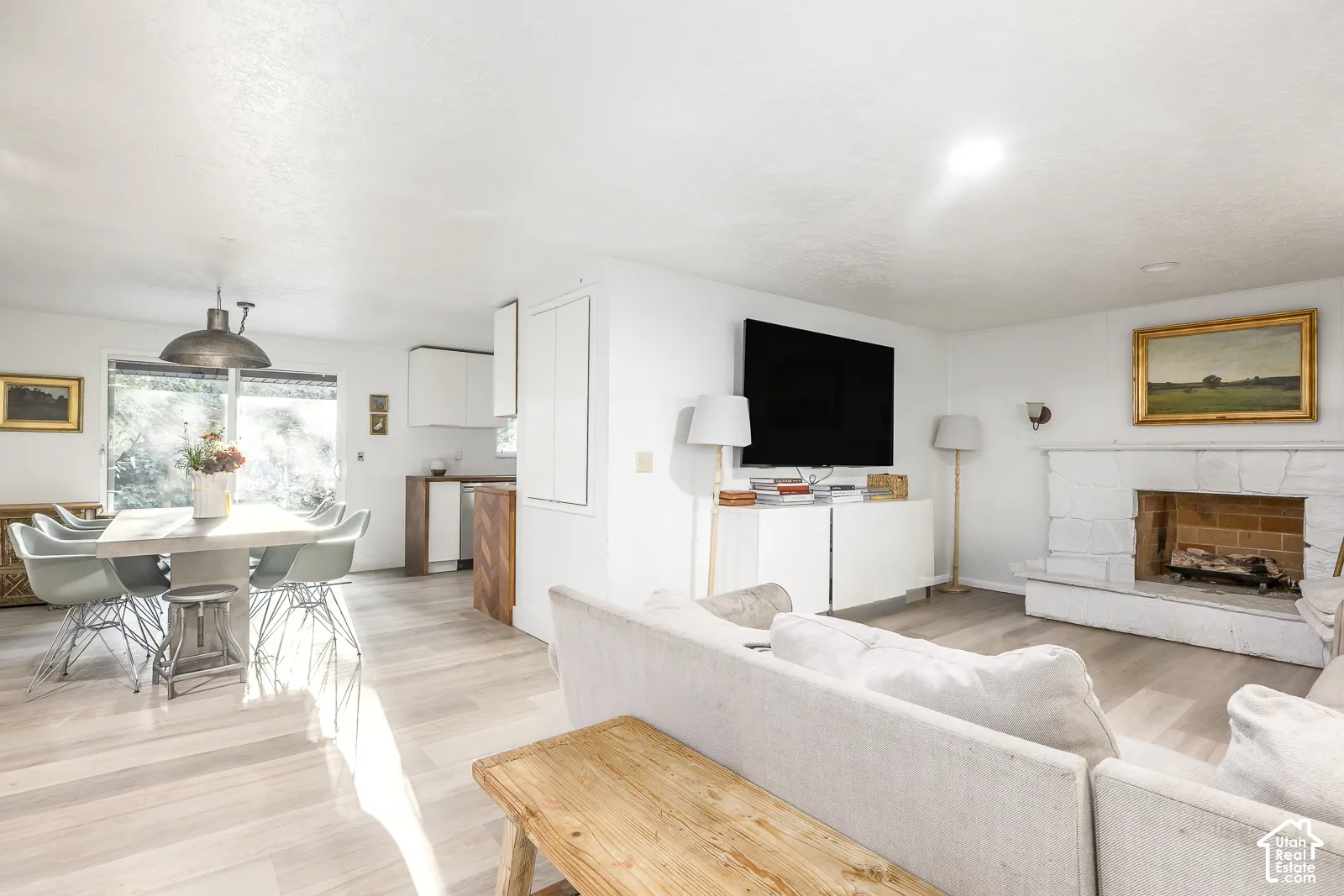 Wood-finish flooring throughout, a stone-clad fireplace, and a kitchen featuring white cabinetry and wood-finish lower cabinetry