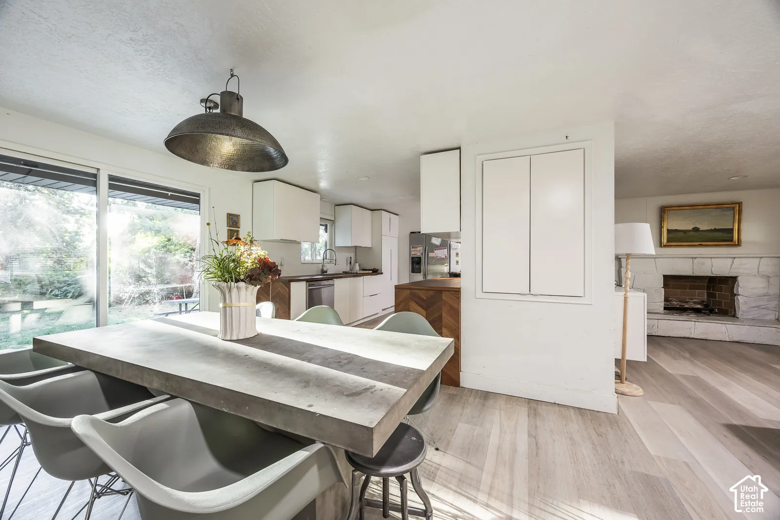 Open-concept living space featuring wood-finish flooring, a white stone fireplace, and a kitchen with white cabinetry