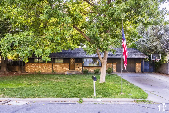 Brick facade, mature trees, attached garage, well-maintained lawn, and paved driveway