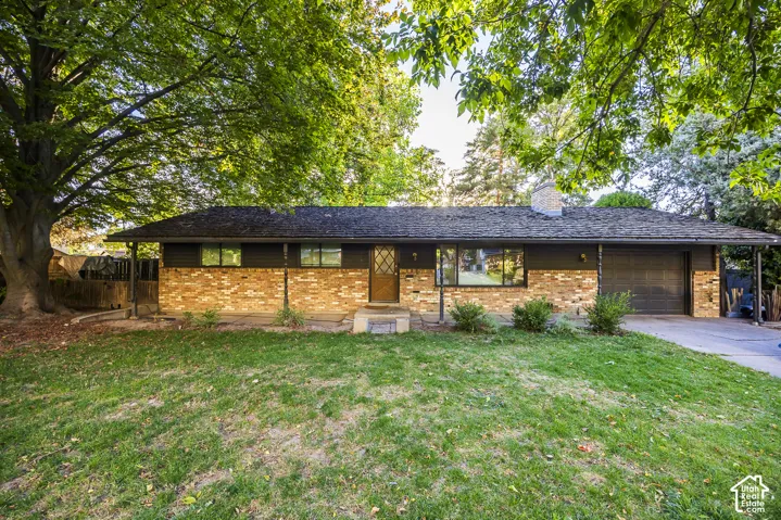 Brick facade with dark siding, single-car garage, front entry with storm door, and mature shade trees