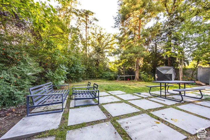 Expansive backyard with a large concrete paver patio, a manicured lawn, and mature trees