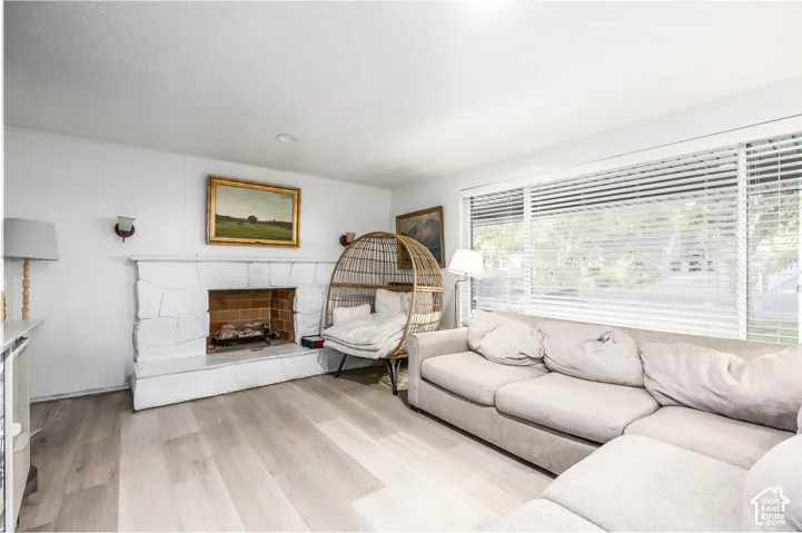 Light wood-finish flooring, stone-clad fireplace with brick firebox, wall-mounted sconces, and extensive window with horizontal blinds