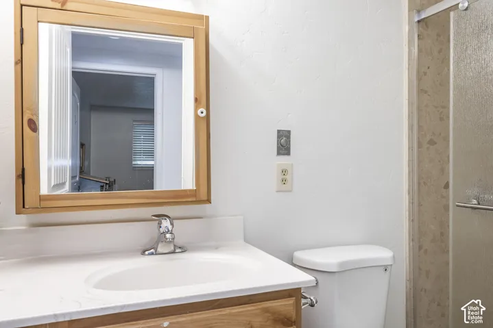 Wood-framed medicine cabinet, integrated sink with chrome faucet, light-toned countertop, and shower enclosure with textured glass