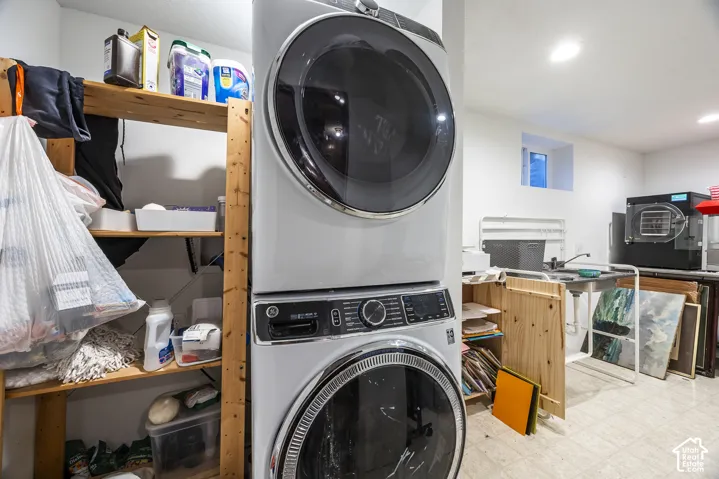 Laundry area featuring a stacked washer and dryer, wood shelving, and a utility sink