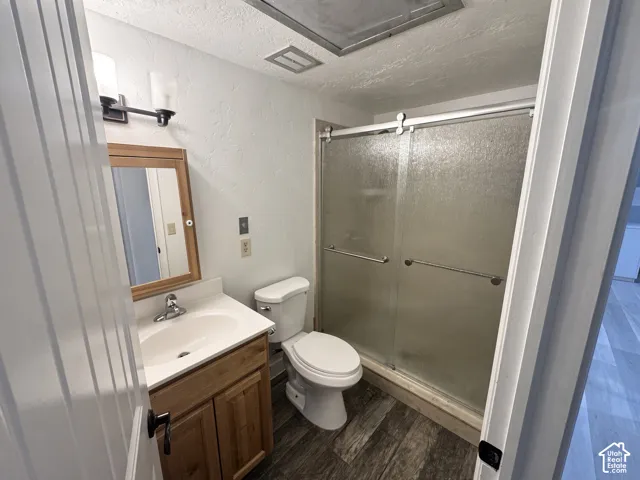 Wood-finish flooring, single vanity with wood cabinetry, glass-enclosed shower with sliding doors, wall-mounted light fixture, and a framed mirror