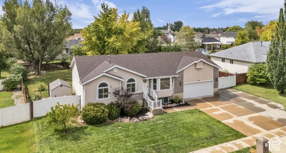 Ranch-style residence featuring a two-car garage, manicured lawn, paved driveway, and established landscaping