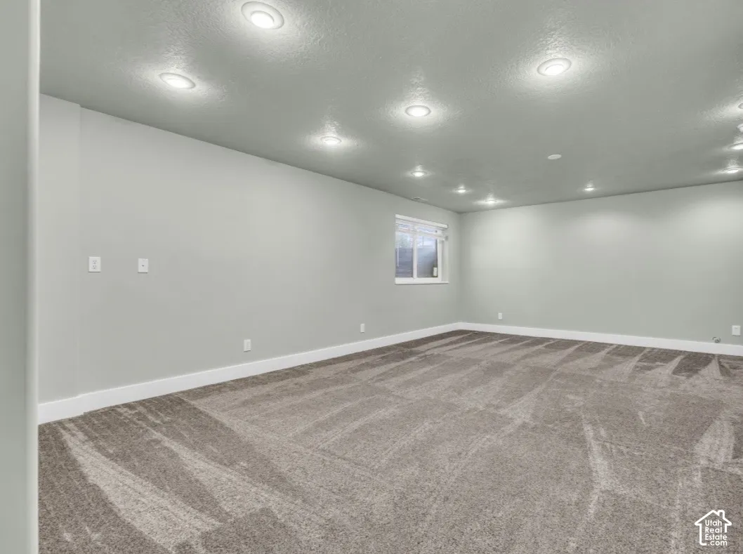 Spacious room with recessed lighting, light gray walls, white trim, and patterned gray carpeting