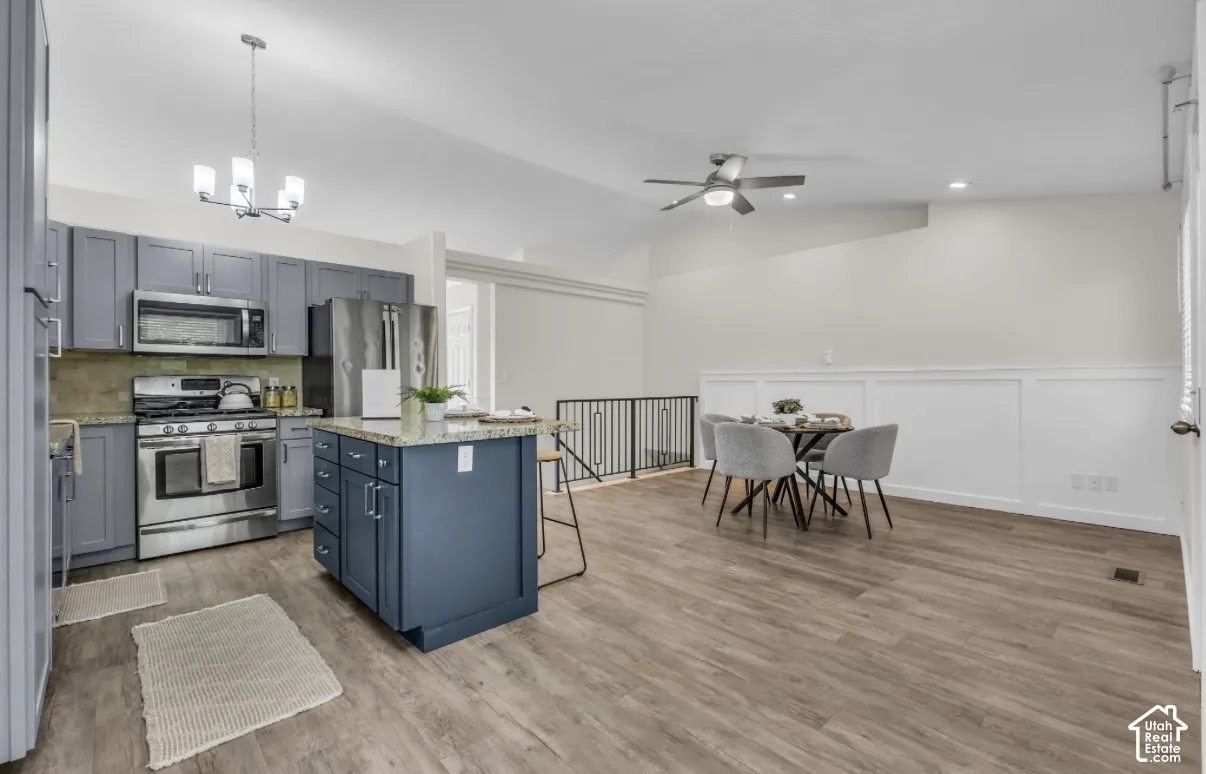 Open-concept living space featuring wood-finish flooring, a kitchen island with granite countertop, stainless steel appliances, and a ceiling fan