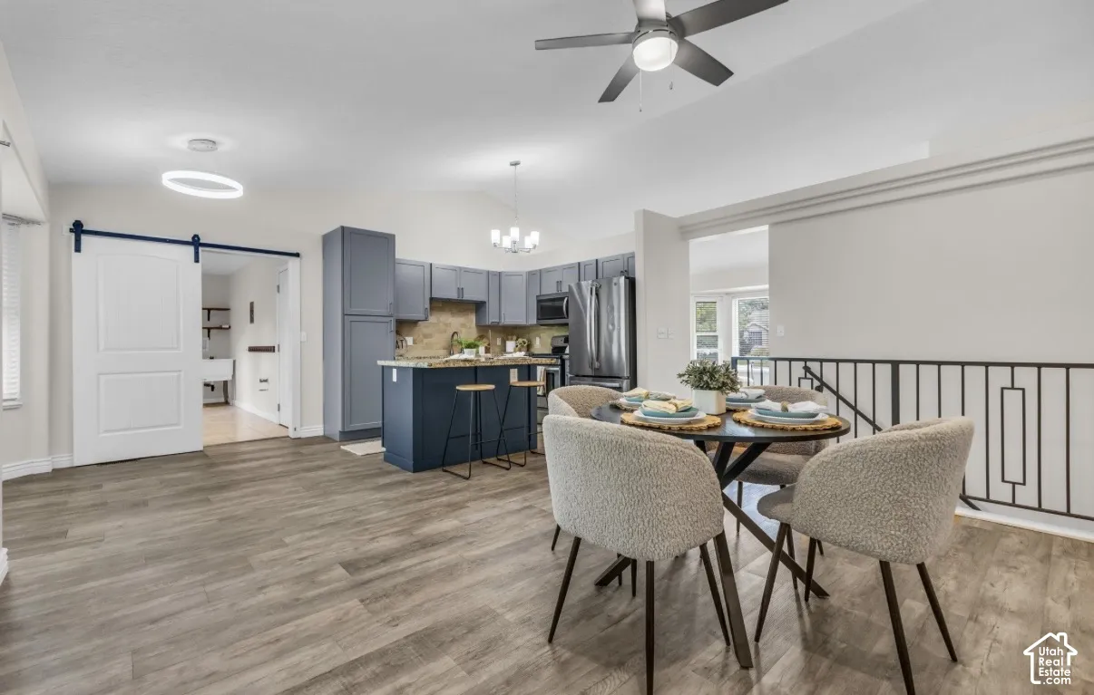Wood-finish flooring throughout, kitchen with blue cabinetry and stainless steel appliances, dining area with a contemporary chandelier, and a black metal railing