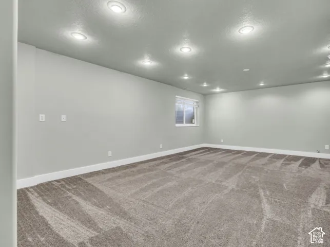Spacious room with recessed lighting, light gray walls, white trim, and patterned gray carpeting