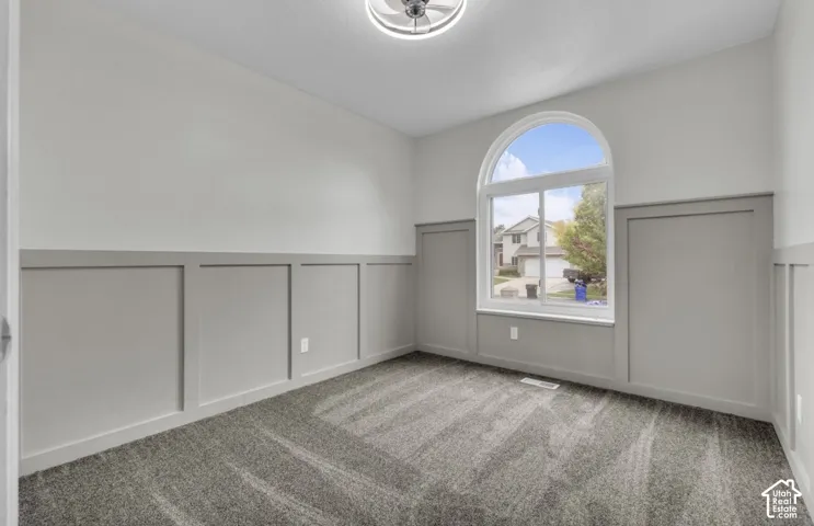Arched window, board and batten wall treatment, ceiling-mounted light fixture, and gray textured carpeting