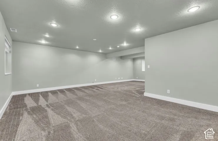 Spacious room featuring neutral carpeting, light-toned walls, and recessed ceiling lighting