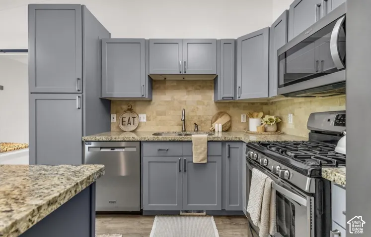 Kitchen featuring gray cabinetry, stainless steel appliances, a tile backsplash, and granite countertops