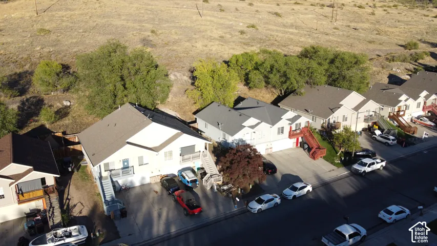 Aerial perspective featuring multi-level residential structures with pitched rooflines and concrete driveways, situated against a backdrop of mature trees and hillside terrain