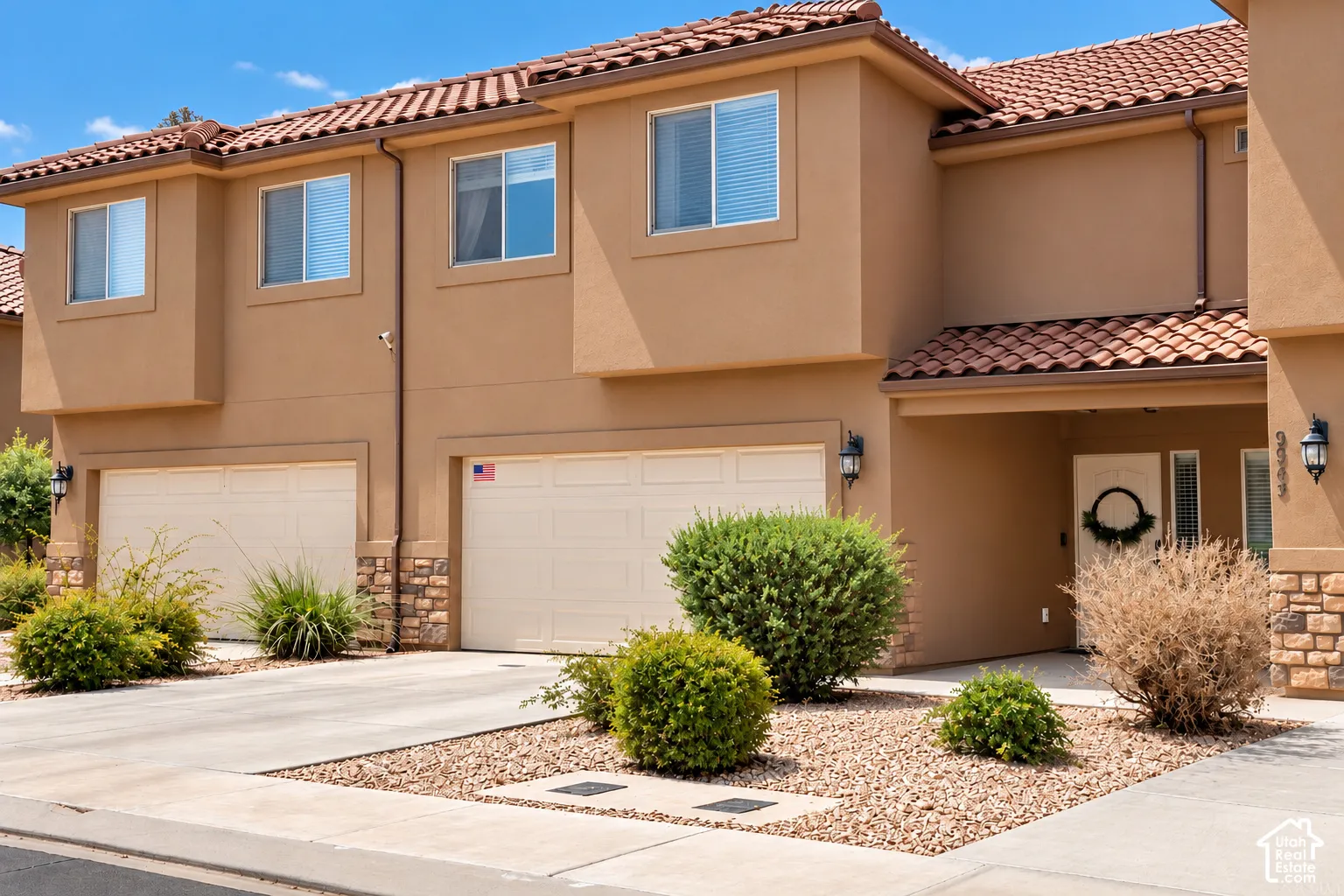 Stucco exterior with a terracotta tile roof, two attached garages, covered entryway, and stone accents