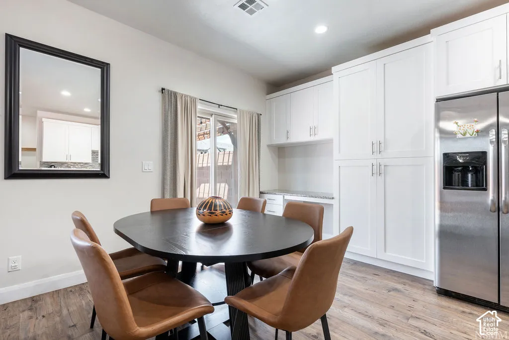 Wood-finish flooring, white cabinetry with silver-tone hardware, stainless steel refrigerator, built-in counter space, and sliding glass door
