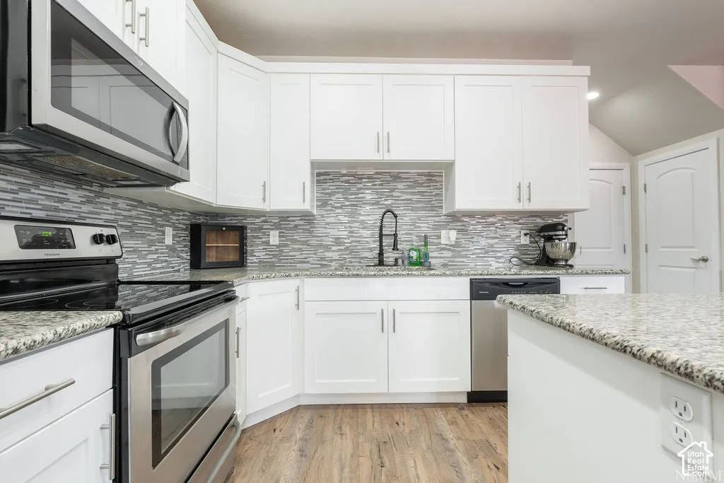 Modern kitchen with white cabinetry, granite countertops, wood-finish flooring, stainless steel appliances, and a tiled backsplash