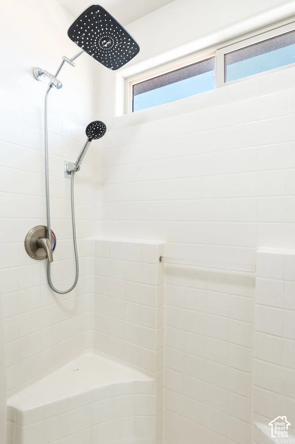 Shower with white rectangular tile surround, dual shower heads, integrated corner bench, and frosted transom window
