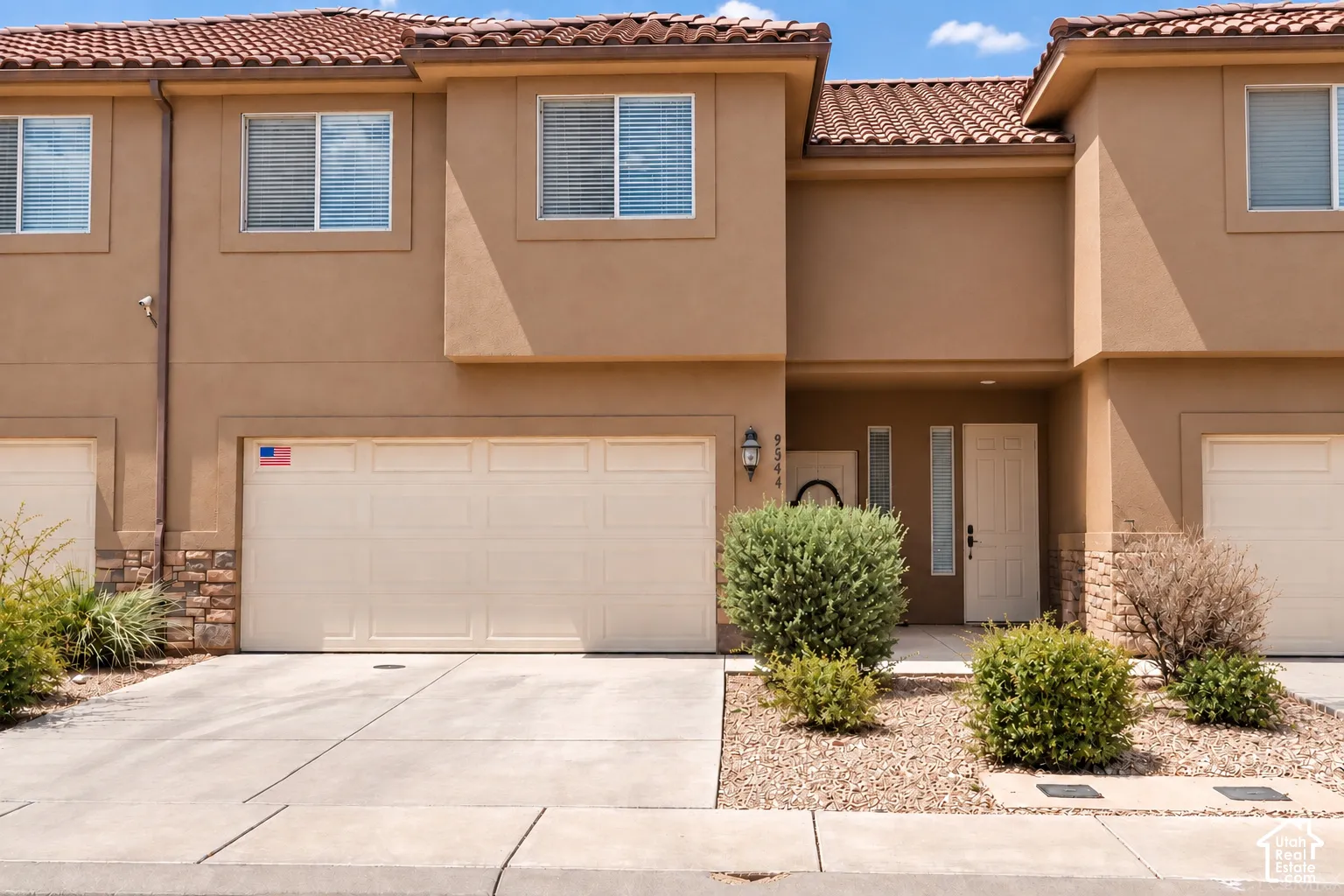 Stucco exterior with stone accents, tiled roof, attached garage, and a concrete driveway