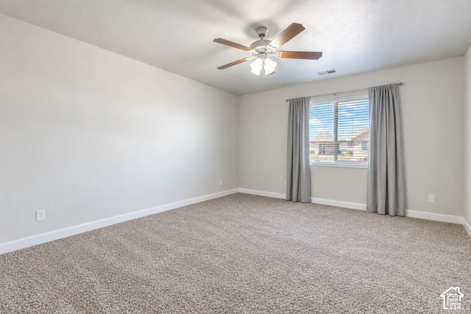 Neutral-toned wall finish, recessed window with horizontal blinds, ceiling fan with integrated lighting, and plush carpet flooring
