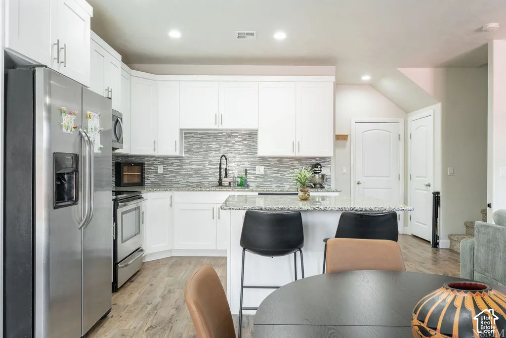 Modern kitchen featuring stainless steel appliances, white cabinetry, a large center island with seating, a textured tile backsplash, and wood-finish flooring