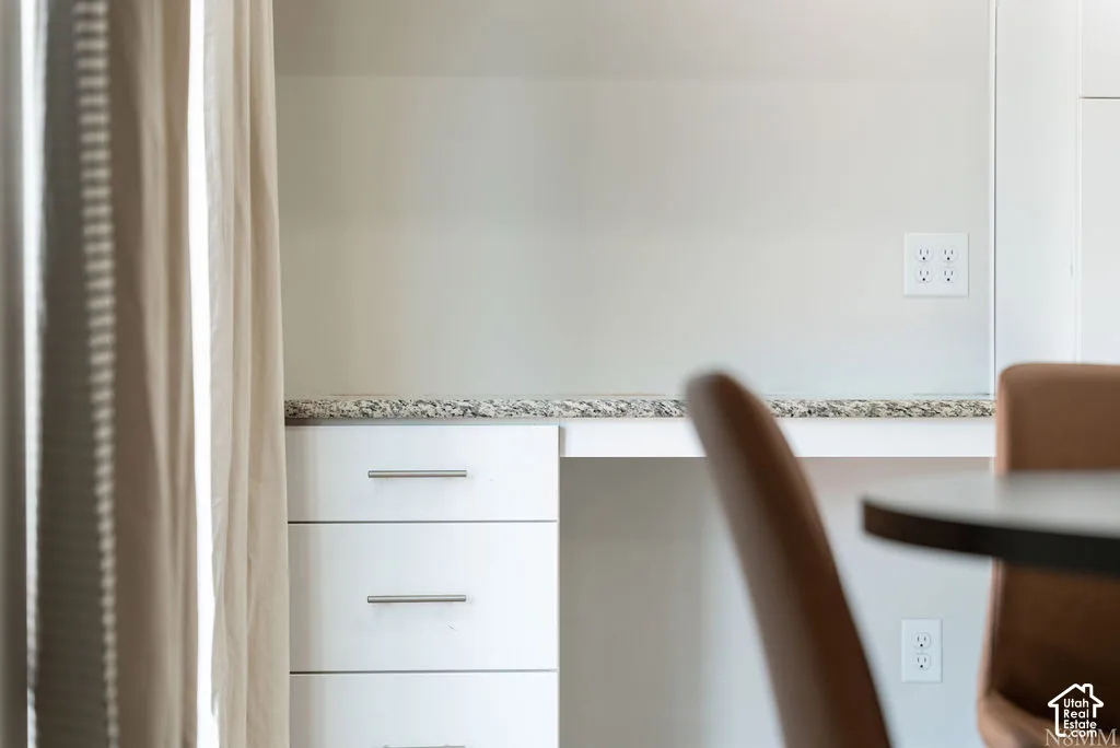 Built-in desk area with a light-toned countertop, white cabinetry featuring modern pulls, and multiple electrical outlets