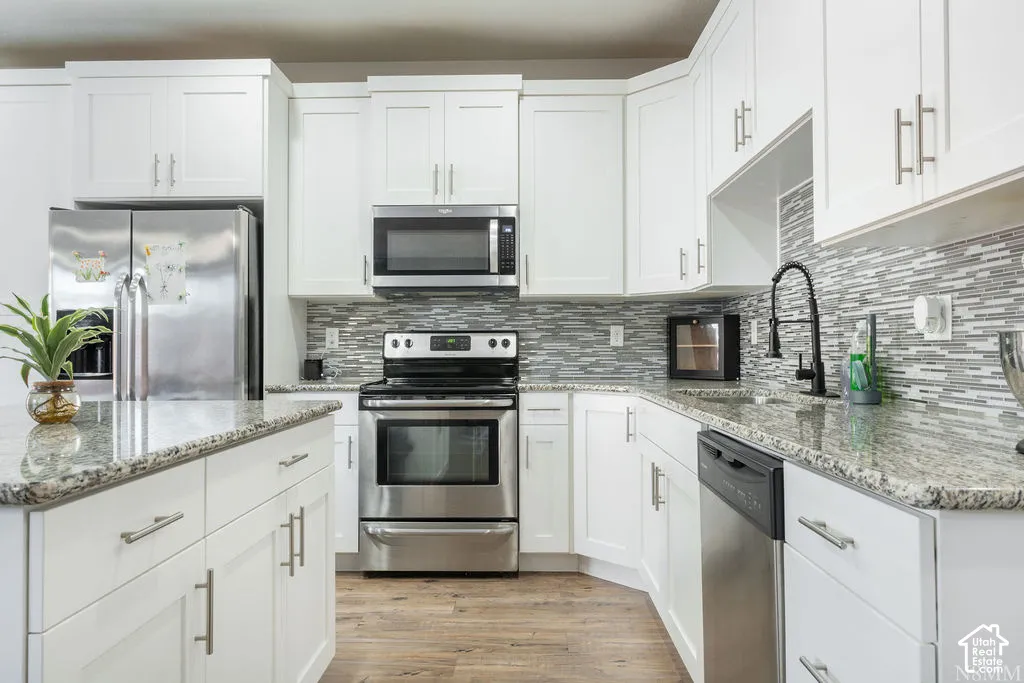 Kitchen featuring white cabinetry, stainless steel appliances, granite countertops, a mosaic tile backsplash, and wood-finish flooring