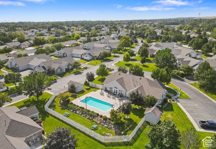Community pool with surrounding patio space, clubhouse building, landscaped grounds, and white picket fencing