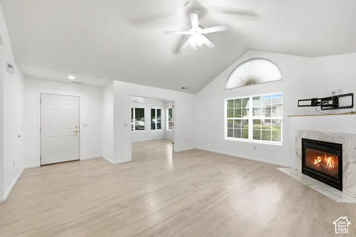 Vaulted ceiling with a ceiling fan, fireplace with a tile surround, large window, arched transom window, and wood-finish flooring