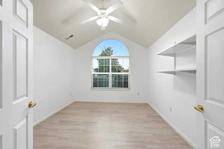Vaulted ceiling with a ceiling fan, arched window, wood-finish flooring, and built-in shelving
