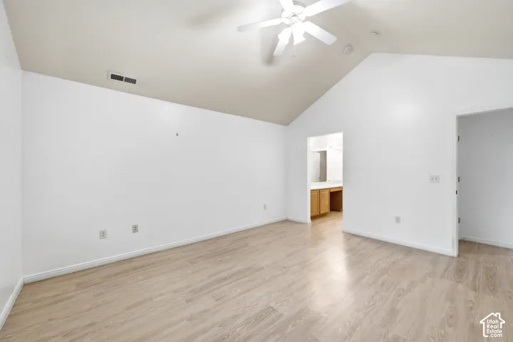 Vaulted ceiling with a ceiling fan, light wood-finish flooring, and an open doorway leading to a vanity area