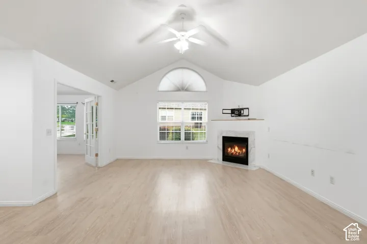 Vaulted ceiling with ceiling fan, wood-finish flooring, corner fireplace with stone surround, arched transom window, and French doors