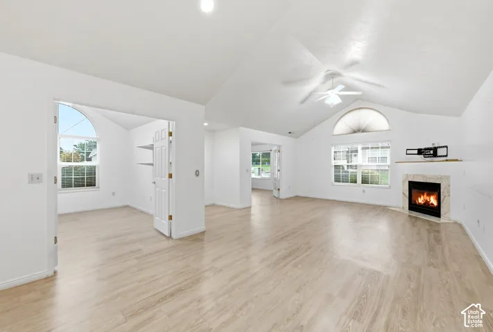 Vaulted ceiling with a ceiling fan, light wood-finish flooring, and a fireplace with a stone surround
