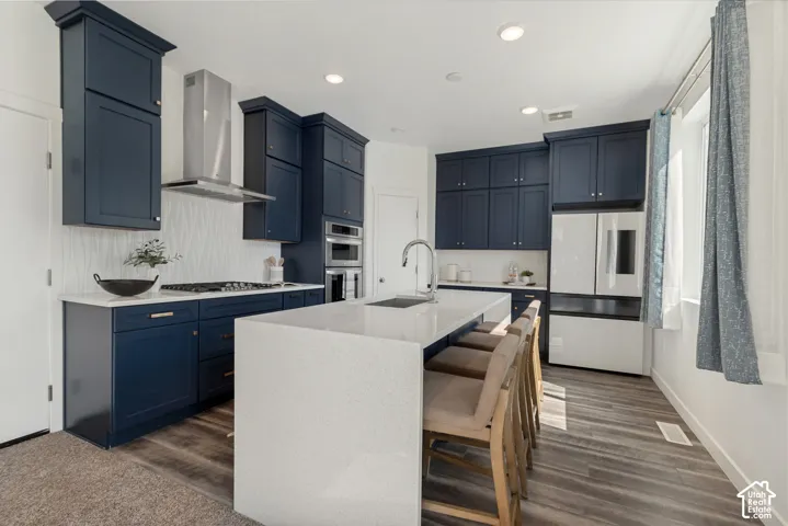 Spacious kitchen featuring deep blue cabinetry, stainless steel range hood, built-in oven, white countertop, and wood-finish flooring