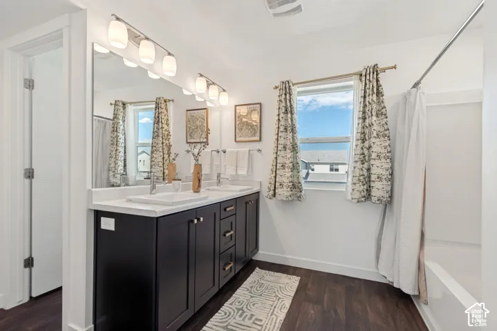 Dual vanity with white undermount sinks, wood-finish flooring, and a shower-over-tub combination